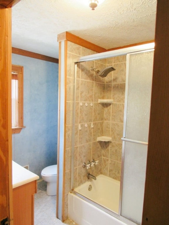 full bathroom with combined bath / shower with glass door, toilet, vanity, tile patterned floors, and a textured ceiling