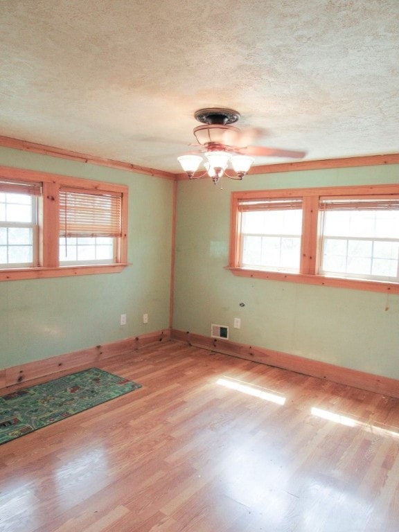 empty room with light wood-type flooring, a textured ceiling, and a chandelier