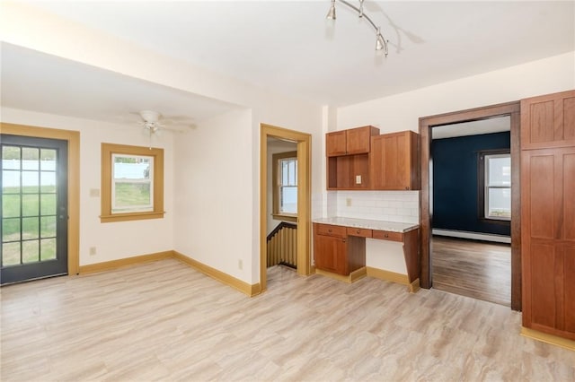 kitchen with light countertops, decorative backsplash, a baseboard heating unit, light wood-style floors, and built in study area