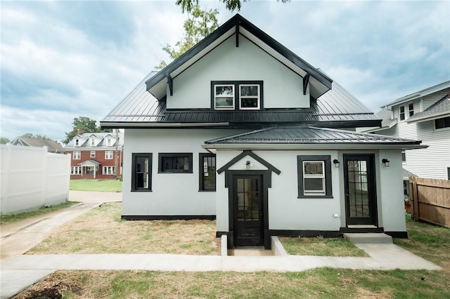 rear view of house featuring a standing seam roof, fence, metal roof, and stucco siding