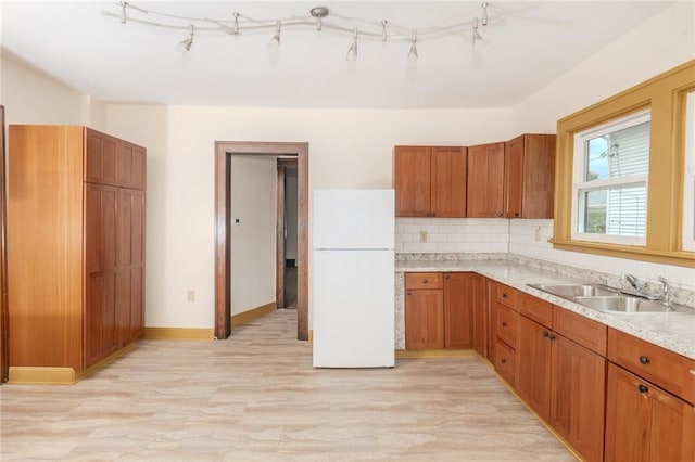 kitchen featuring brown cabinets, backsplash, freestanding refrigerator, a sink, and baseboards