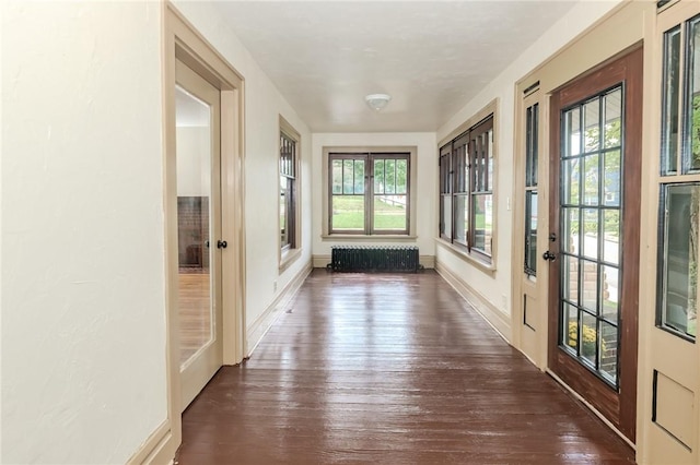 interior space with dark wood-type flooring, baseboards, a healthy amount of sunlight, and radiator heating unit