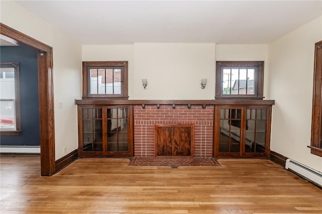 unfurnished living room featuring baseboard heating, a wealth of natural light, and light wood-style floors