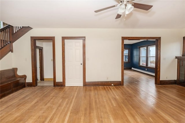 unfurnished room with a baseboard radiator, light wood-style floors, a ceiling fan, baseboards, and stairs