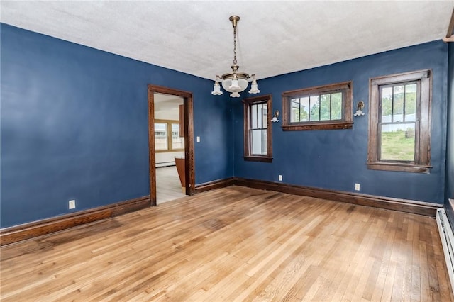 spare room with baseboards, hardwood / wood-style floors, a wealth of natural light, and an inviting chandelier