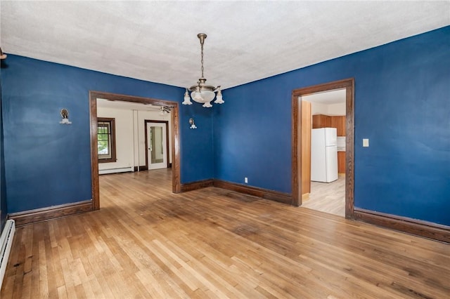 empty room featuring a baseboard heating unit, a chandelier, wood finished floors, and baseboards