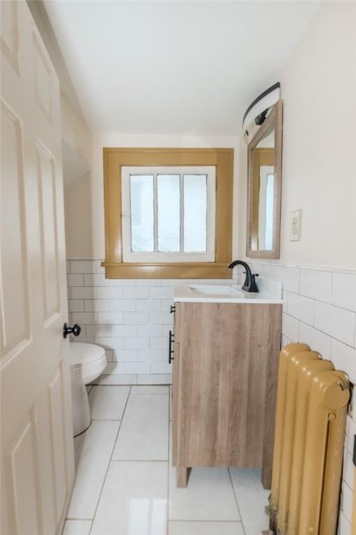 half bath with toilet, radiator heating unit, tile walls, and tile patterned flooring