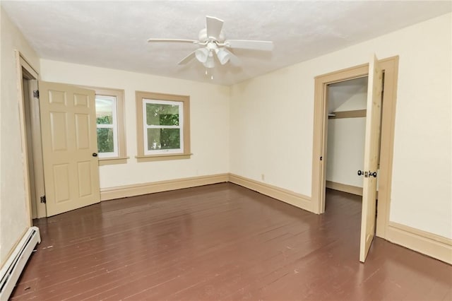 unfurnished bedroom featuring a baseboard radiator, dark wood-type flooring, baseboards, a closet, and a walk in closet