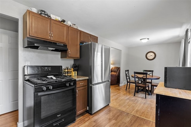 kitchen featuring black gas range oven, stainless steel fridge, and light hardwood / wood-style floors