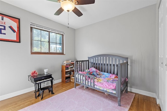 bedroom featuring light hardwood / wood-style floors, a nursery area, and ceiling fan