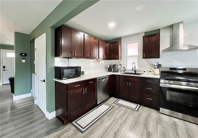 kitchen featuring appliances with stainless steel finishes, decorative backsplash, light hardwood / wood-style floors, wall chimney exhaust hood, and sink