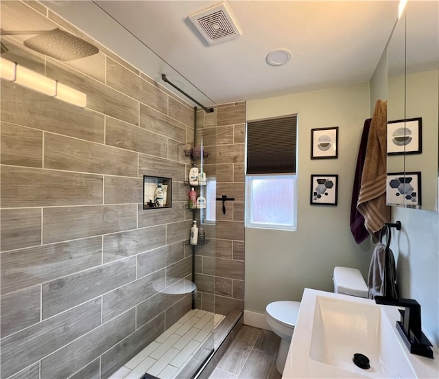 bathroom featuring a tile shower, sink, hardwood / wood-style flooring, and toilet