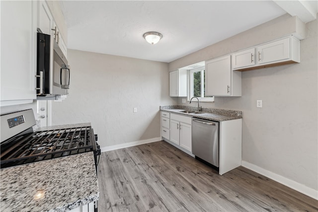 kitchen featuring white cabinetry, appliances with stainless steel finishes, light stone counters, light hardwood / wood-style floors, and sink