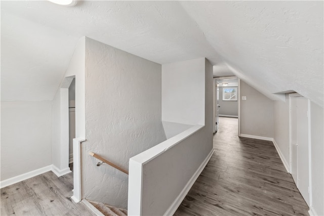 hallway with a textured ceiling, lofted ceiling, and wood-type flooring