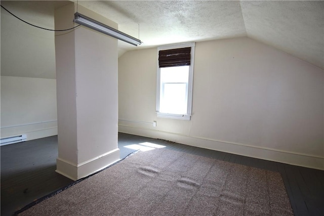 additional living space featuring a baseboard radiator, vaulted ceiling, a textured ceiling, wood finished floors, and baseboards