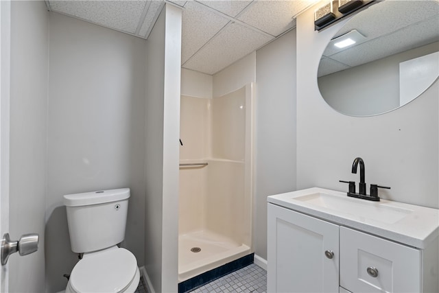 bathroom with a drop ceiling, tile patterned floors, vanity, toilet, and walk in shower