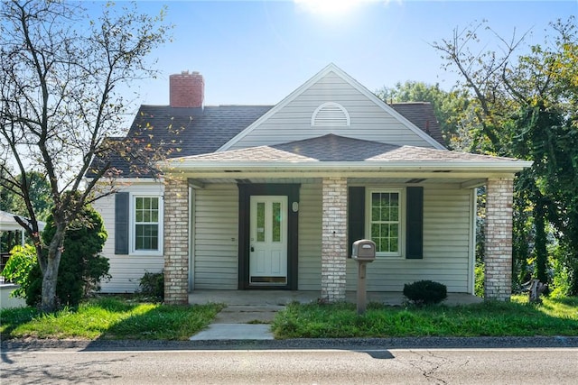 view of front of property with roof with shingles, a porch, and a chimney