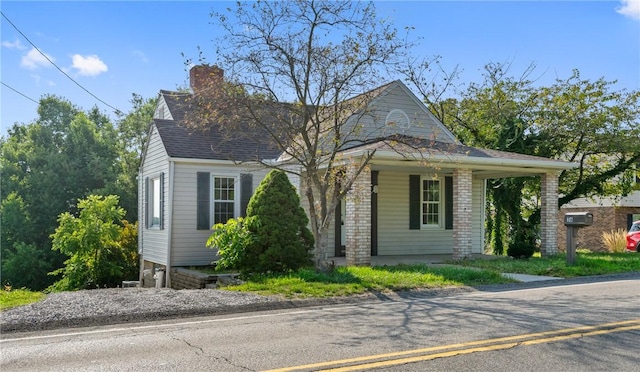 view of front of property with a shingled roof, brick siding, a porch, and a chimney