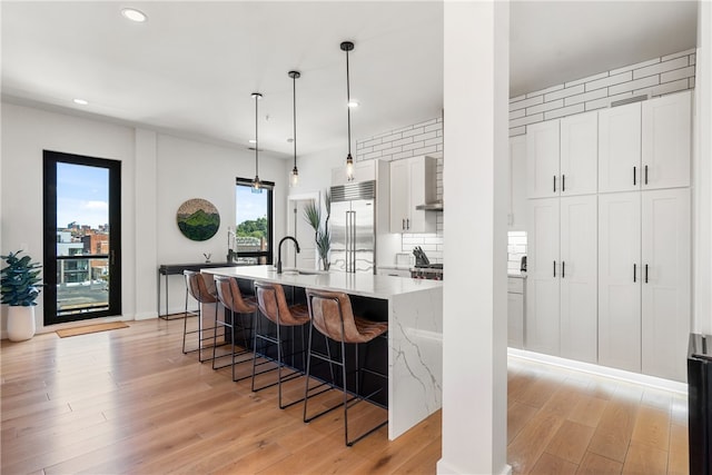 kitchen featuring pendant lighting, stainless steel built in fridge, a kitchen breakfast bar, and white cabinetry