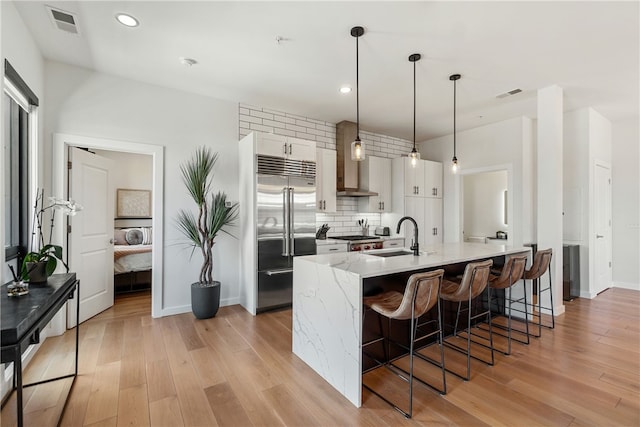 kitchen with a sink, visible vents, white cabinetry, stainless steel built in refrigerator, and decorative light fixtures