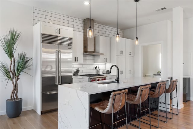 kitchen featuring light stone counters, visible vents, white cabinets, stainless steel built in fridge, and a center island with sink