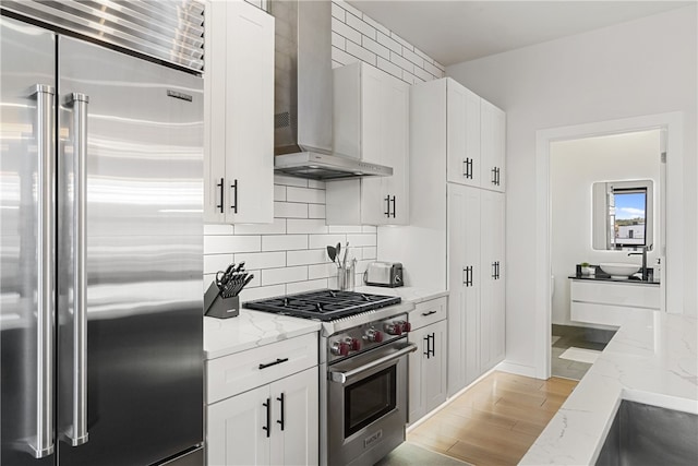 kitchen with premium appliances, white cabinets, wall chimney range hood, and light stone counters