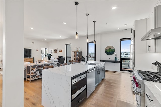 kitchen featuring hanging light fixtures, a kitchen island with sink, stainless steel appliances, white cabinetry, and a sink