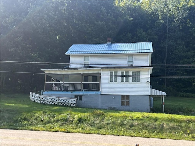 back of house featuring metal roof, a yard, a chimney, and a forest view