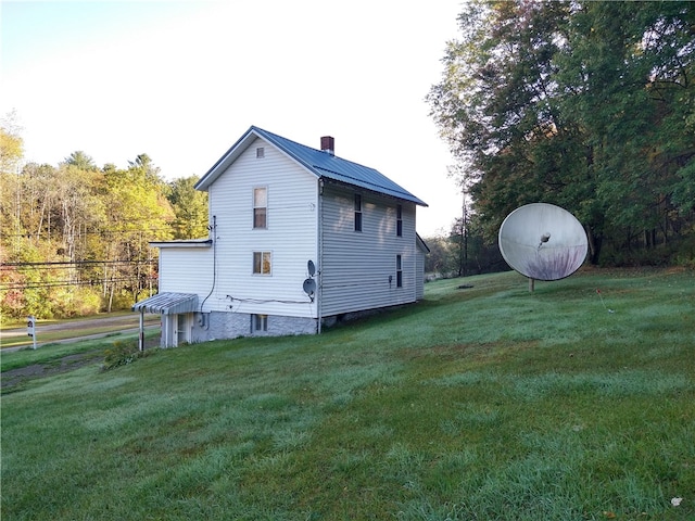 view of side of property featuring metal roof, a lawn, and a chimney