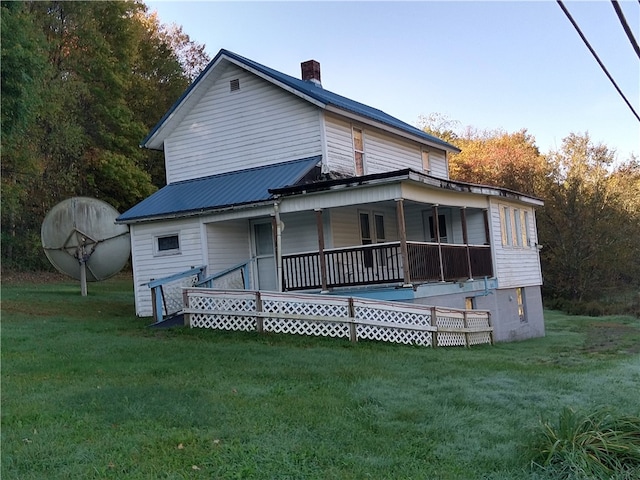 rear view of house featuring metal roof, a yard, a porch, and a chimney