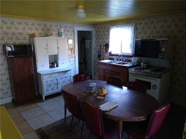 kitchen featuring white cabinets, light tile patterned flooring, a sink, and wallpapered walls