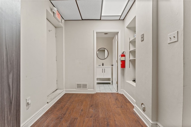 interior space featuring a drop ceiling, wood-type flooring, and built in shelves