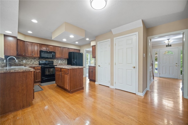 kitchen with light hardwood / wood-style flooring, sink, black appliances, a center island, and tasteful backsplash