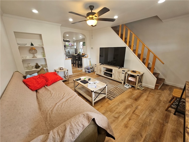 living room with ceiling fan, built in shelves, crown molding, and hardwood / wood-style floors