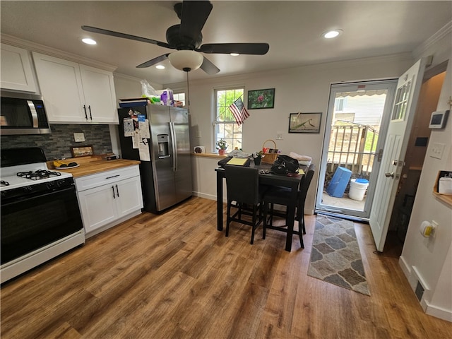 kitchen featuring appliances with stainless steel finishes, hardwood / wood-style floors, ornamental molding, butcher block countertops, and ceiling fan