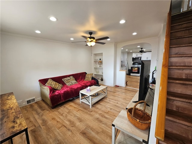 living room featuring ceiling fan, light wood-type flooring, crown molding, and built in shelves