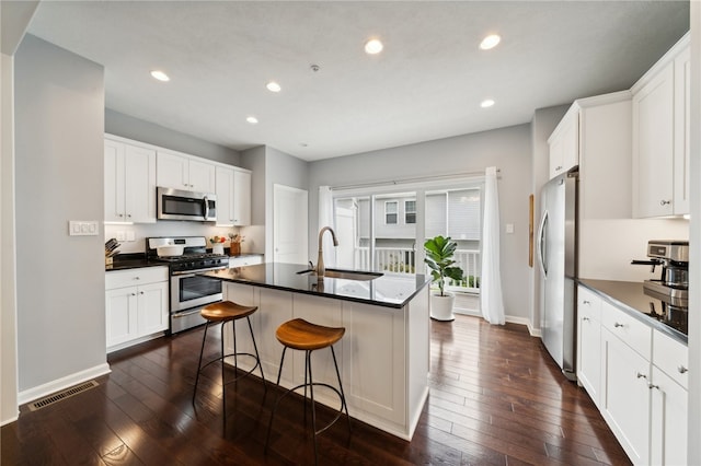 kitchen featuring appliances with stainless steel finishes, sink, a center island with sink, dark hardwood / wood-style flooring, and a breakfast bar