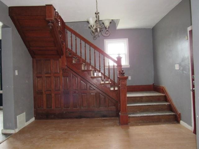 stairway featuring baseboards, wood finished floors, and a notable chandelier