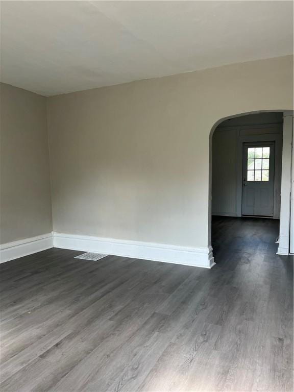 spare room with arched walkways, dark wood finished floors, and baseboards