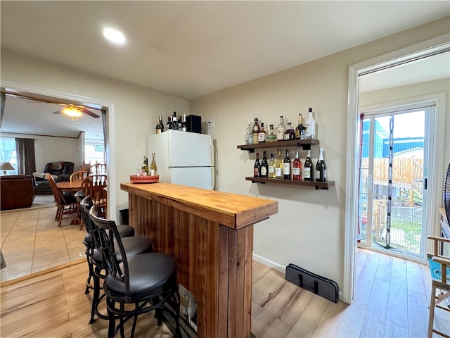 bar with white fridge, plenty of natural light, light hardwood / wood-style floors, and ceiling fan