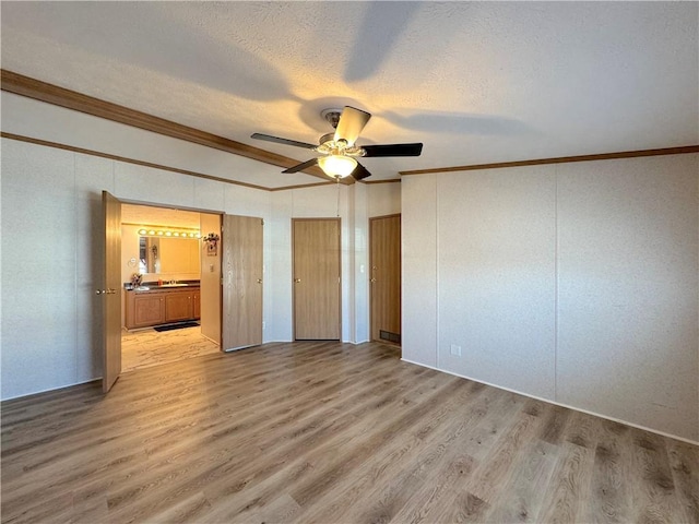 unfurnished bedroom with a ceiling fan, ensuite bath, light wood-style flooring, ornamental molding, and a textured ceiling