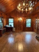 unfurnished living room featuring lofted ceiling, wooden walls, a notable chandelier, and hardwood / wood-style floors