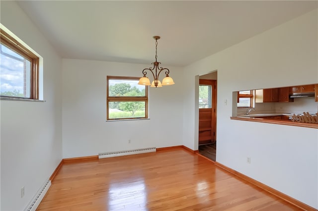 unfurnished dining area with sink, a notable chandelier, a baseboard radiator, and light wood-type flooring