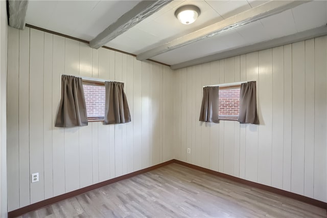 spare room featuring beam ceiling, plenty of natural light, and light wood-type flooring