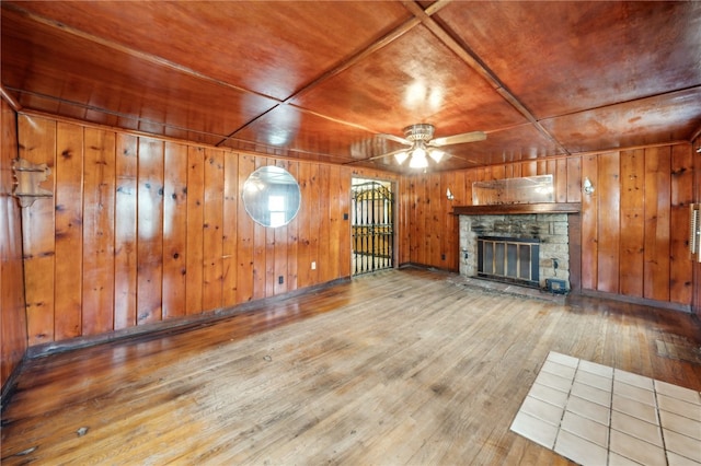 unfurnished living room with hardwood / wood-style floors, a stone fireplace, wooden ceiling, and wood walls