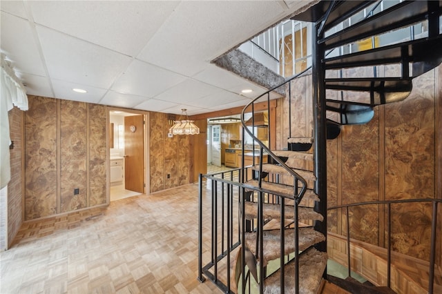 staircase with a paneled ceiling, parquet flooring, and wooden walls