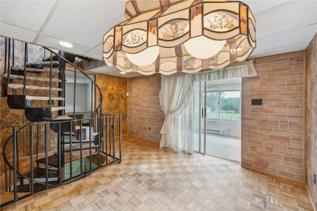 interior space featuring a drop ceiling, parquet flooring, brick wall, and a baseboard radiator