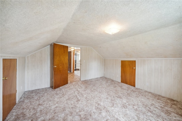 additional living space with a textured ceiling, light colored carpet, and lofted ceiling