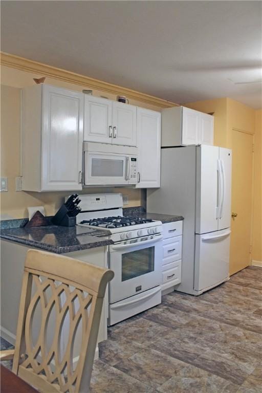 kitchen featuring white appliances, white cabinetry, and dark stone countertops