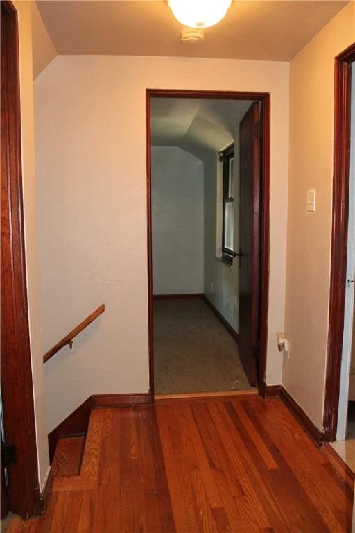 hallway with baseboards, vaulted ceiling, and wood finished floors